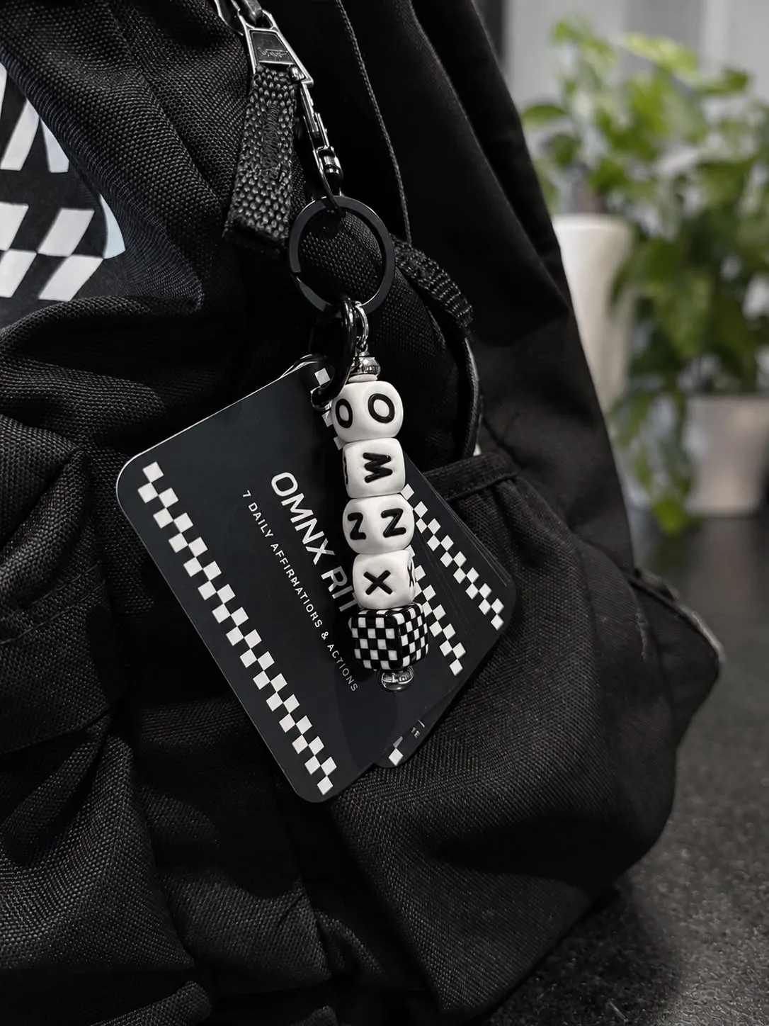 The set hanging from the strap of a black backpack, the beaded OMNX charm in front of the title card