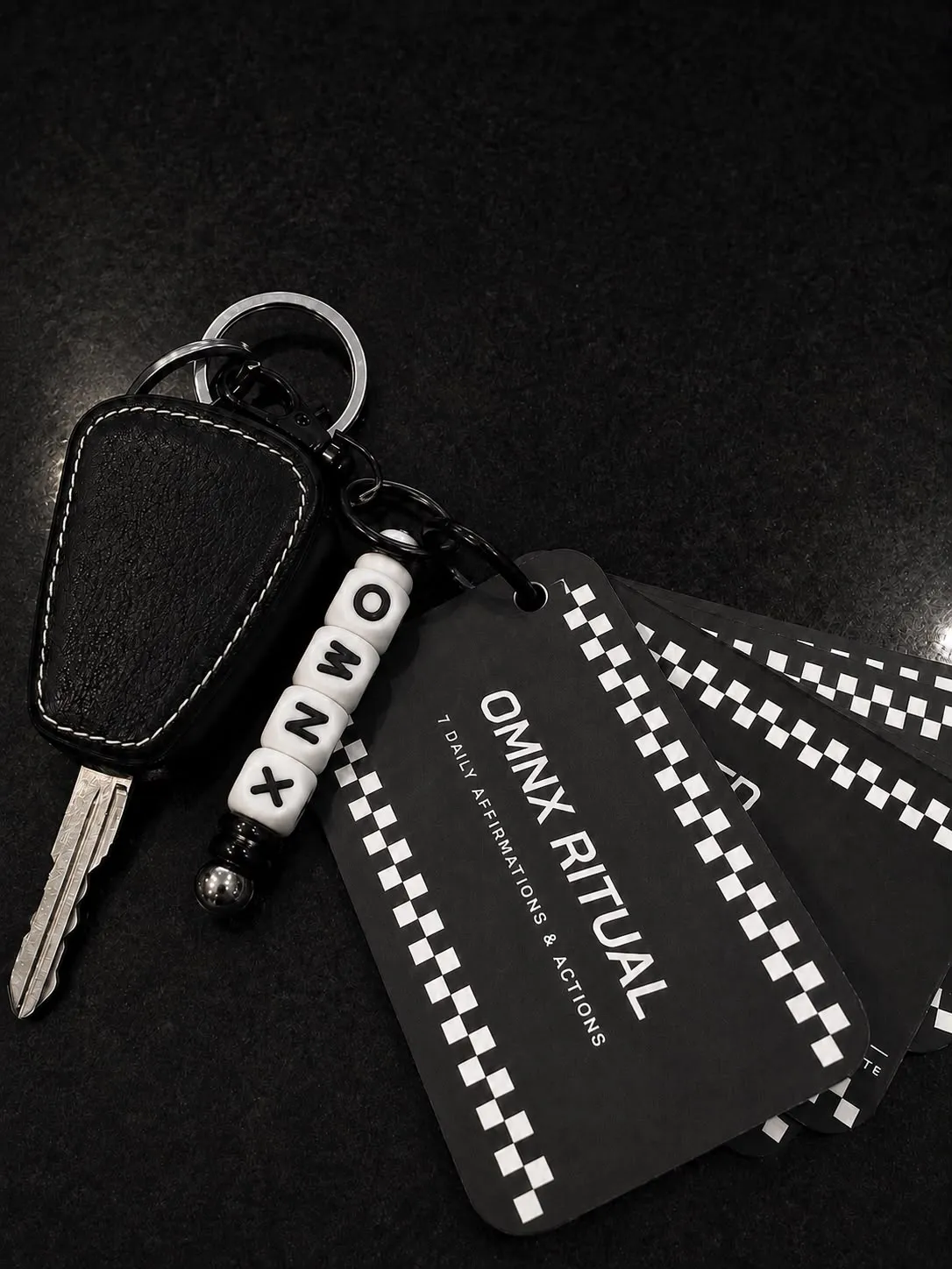 The set sharing a split ring with a car key and a plain black fob cover, the beaded OMNX charm to the left of the fanned cards