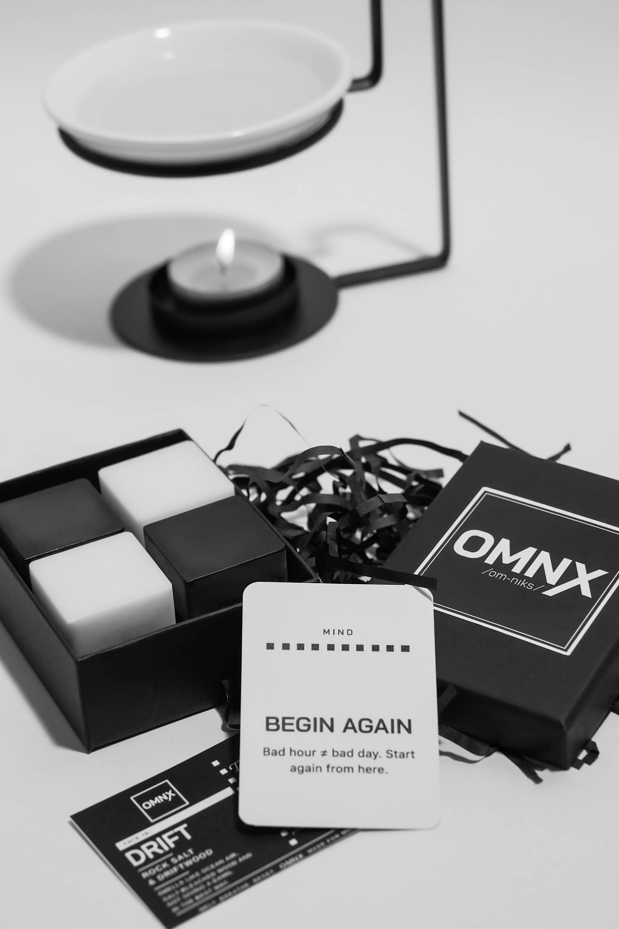 The open Drift box holding its four wax squares, two white and two black, with the OMNX lid behind and the Drift scent card and an OMNX RESET card in front