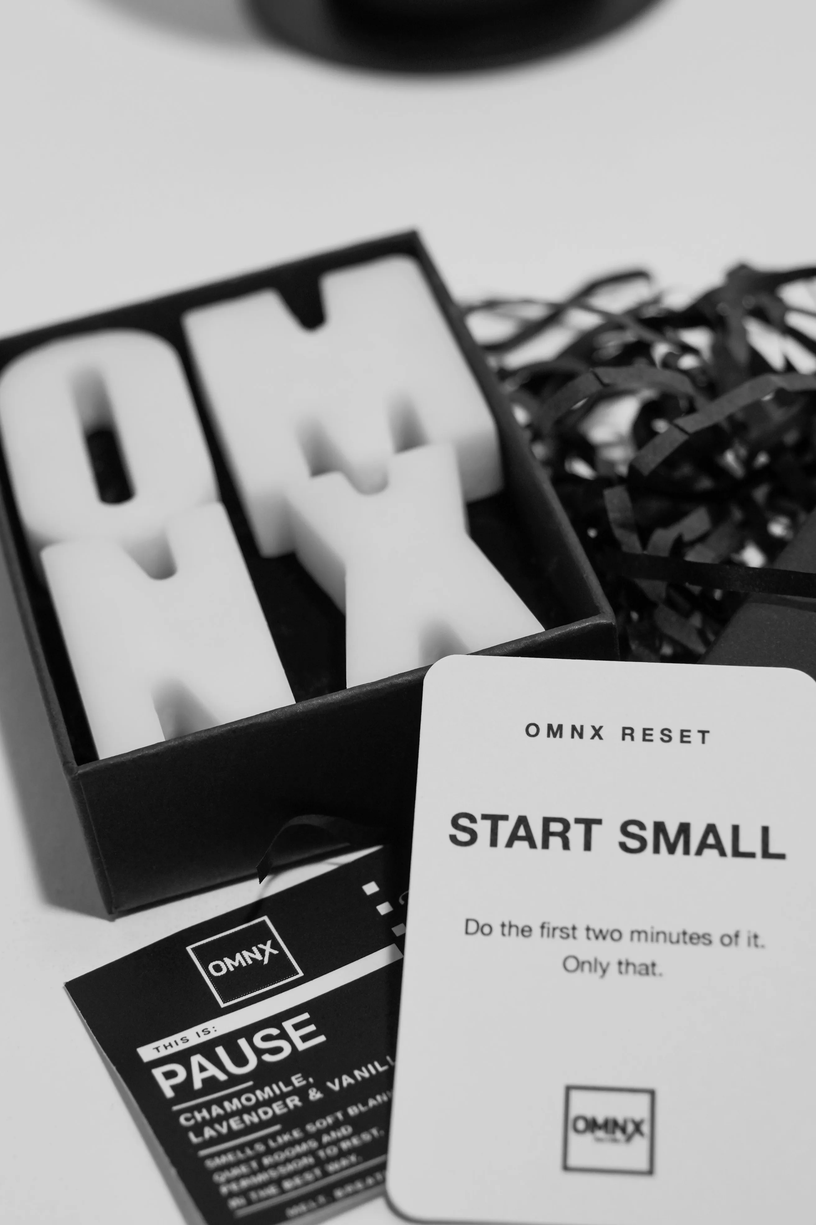 The open Pause box holding the four pale wax letters, with the Pause scent card and an OMNX RESET card in front